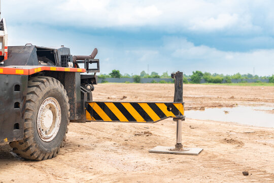 Close-up of a heavy-duty mobile crane's hydraulic outrigger extended and firmly planted on a metal base plate at a muddy construction site.