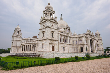 Fototapeta premium Front view of Victoria Memorial, the iconic white marble monument in Kolkata, India, surrounded by lush green gardens under a clear blue sky.
