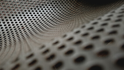 Close up of a grey perforated metal sheet texture. Abstract industrial background with a pattern of round holes and selective focus © Jassem