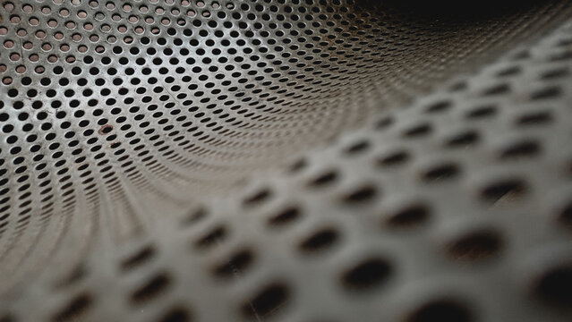 Close up of a grey perforated metal sheet texture. Abstract industrial background with a pattern of round holes and selective focus