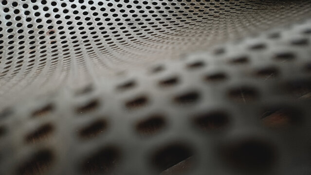Close up of a grey perforated metal sheet texture. Abstract industrial background with a pattern of round holes and selective focus