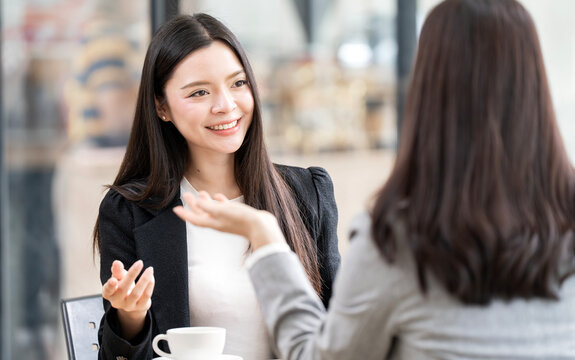Smiling Asian businesswoman listening to her colleague during meeting.
