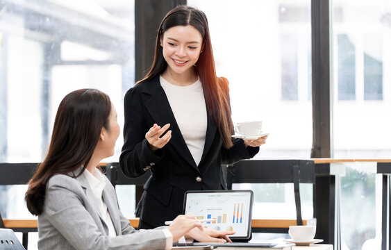 Asian businesswomen analyzing financial charts on tablet in office.
