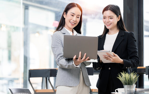 Two smiling Asian businesswomen working together with laptop in office.