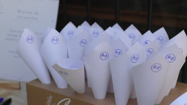 Wedding decoration setup with white paper cone favors stamped with monogram initials on wooden display table