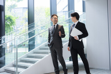 新緑のオフィスの窓際で会話する若手ビジネスマンと上司、取引先のコミュニケーション商談や指導ojtなどの仕事イメージの全身広角 © kapinon