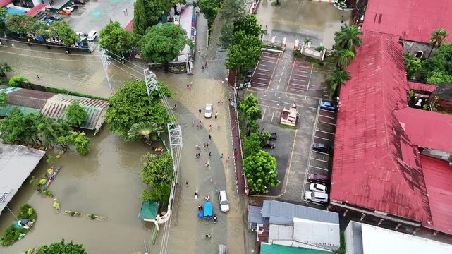 Extreme weather and natural disaster drone footage of flooded provincial town in the Philippines during a heavy monsoon rainstorm - Top-down view of people wading