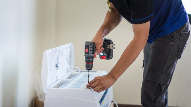 Professional technician installing air conditioner unit with power drill, Repairman working on air conditioning maintenance and installation, Technician using drill for air conditioner wall mounting
