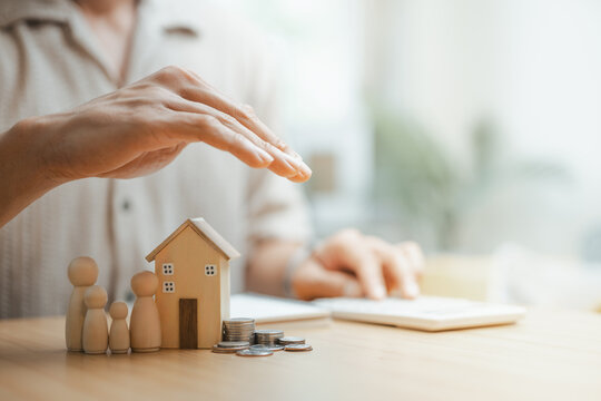 Family protection and life insurance concept with miniature house, family figures, and savings coins under a protective hand. Represents financial security, insurance coverage, beneficiaries.