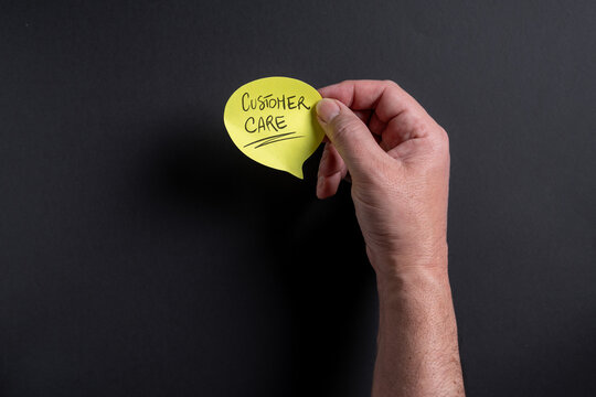 Male hand holding yellow speech bubble about customer care on dark background