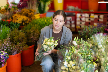 Girl salesman takes out bunch of eustoma from showcase, creates bouquets, combines flowers and decorative herbs. Supply and demand, assortment of flowers for ceremonial and ritual bouquets. © JackF