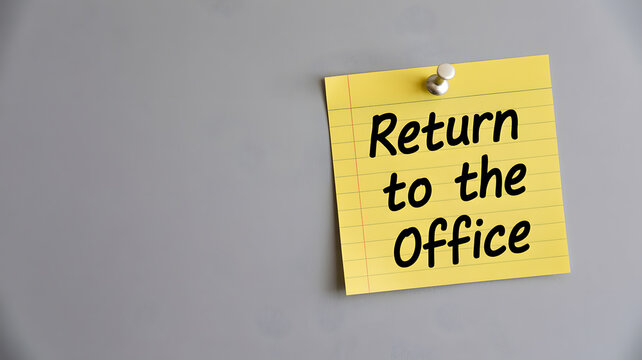 A yellow sticky note with return to the office message on a gray background