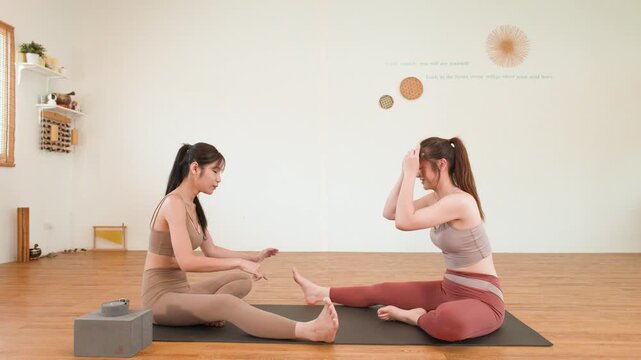 Asian Yoga Instructor Guiding Student Through Leg Stretching Exercises in Studio
