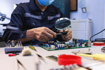 Obraz premium Technician inspecting a circuit board with a magnifying glass at an electronics repair workbench surrounded by tools and components.