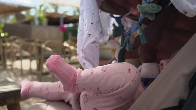 Baby in a stroller at a beach club with toys hanging overhead