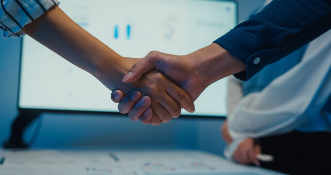 Close up multiracial group young Asia businesspeople in smart casual wear discussing business shaking hand together while stand in modern night office. Partner cooperation, coworker teamwork concept.