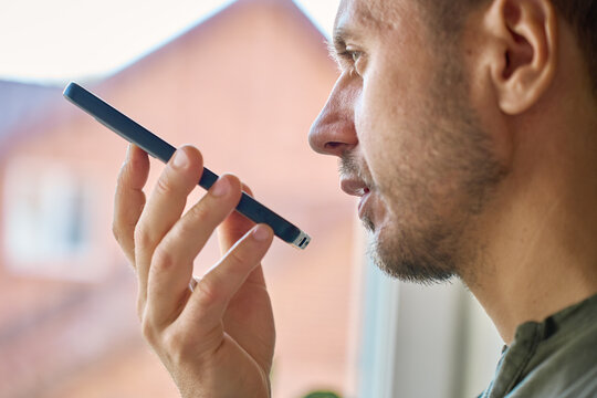 Closeup side view of man speaking into smartphone near window in daylight. Concept of voice message mobile communication and everyday technology use.