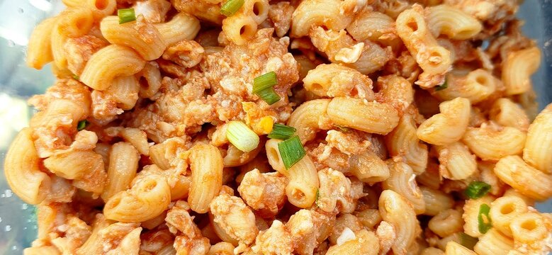 Close-up shot of delicious stir-fried macaroni with egg, minced pork, and tomato sauce, sprinkled with chopped green onions. Tasty homemade comfort food concept.