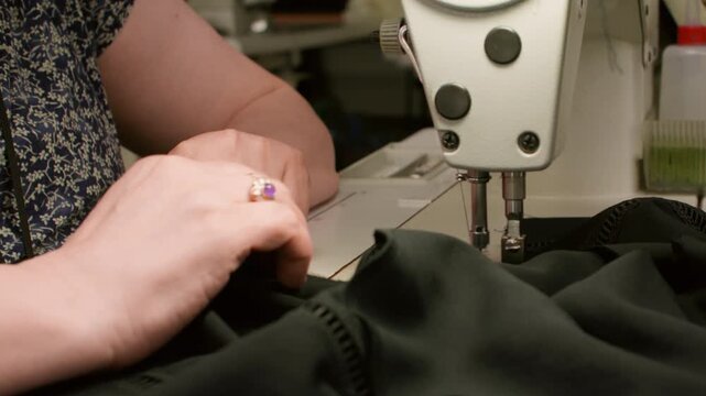 Seamstress occupation. Textile craft. Female hand sewing black clothes on stitching machine. Making thread seam on fabric equipment.