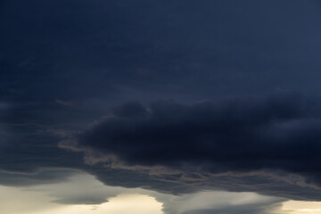 Obraz premium Dark brooding cloudscape with massed storm clouds and pale diffused light breaking through lower cloud layers