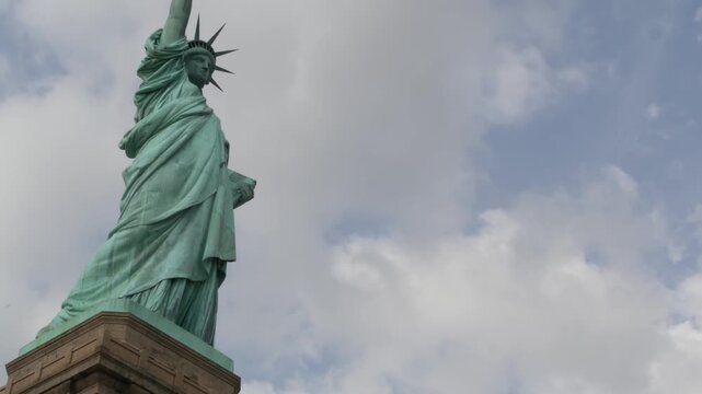 Statue of Liberty on Liberty Island, New York, United States. Blue cooper monument, symbol of democracy and patriotism near Manhattan, NYC USA. Clouds on sky. American independence. Torch and crown.
