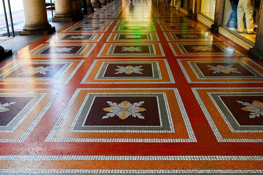 colorful yellow, red and gray shiny terrazzo floor with ceramic mosaic inlay. square pattern. worn repaired surface. covered exterior corridor in genoa, italy. art, architecture and travel concept.