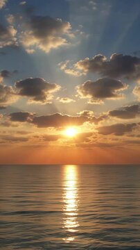Beautiful golden sunset over a calm ocean with sunbeams breaking through the clouds and reflecting on the water. Vertical video