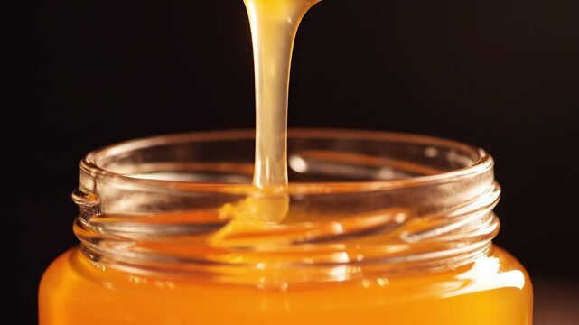 Close up of a silver spoon scooping fresh golden honey from a glass jar
