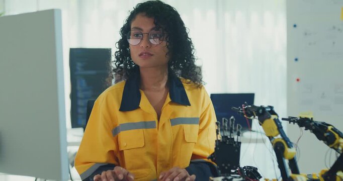 Young African American female robotics engineer coding AI software for robotic arm in laboratory. Embedded system, firmware testing, machine learning, industrial automation, future technology concept.