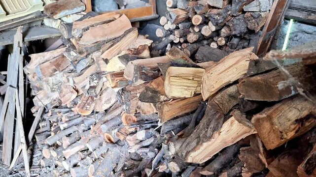 A large pile of chopped firewood stacked inside a rustic woodshed. Natural wooden textures, organized storage, and preparation for winter heating in a rural setting