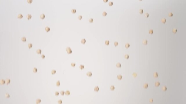 Dried raw Garbanzo Beans Chickpeas raining down on a white backdrop in slow motion close up macro.