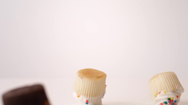 Pastel frosted bite-size cupcakes dropping and bouncing across white seamless backdrop in high speed slow motion. bridal shower brunch posts, bakery party platter ads, dessert table content.