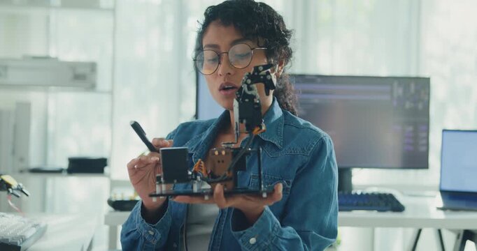 Young African American female robotics engineer discussing mechanical part on video call and looking at camera in laboratory. Remote work, virtual training, online meeting, future technology concept.