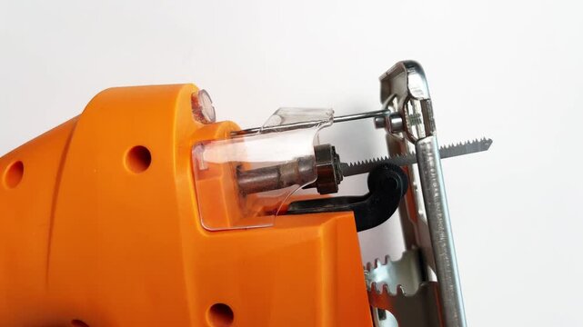 Close-up on a white background of an orange jigsaw spinning, focus on a serrated blade. Concept of working tools, repair, sawing of boards and laminate, power tools. High quality 4k footage