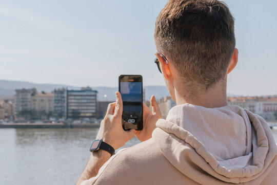 Young male traveler taking smartphone photo of Budapest cityscape across the Danube River