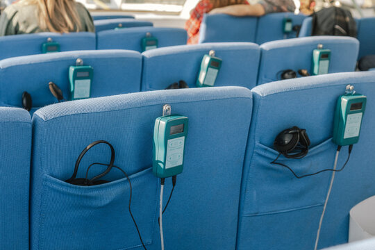Close-up of blue passenger seats equipped with personal audio guide devices and wired headphones for multilingual sightseeing tours and travel experiences