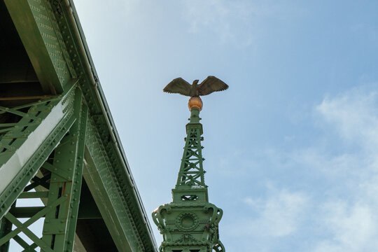 Ornamental eagle sculpture atop historic green steel bridge tower against blue sky