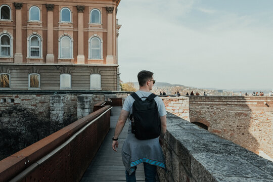 Male traveler with backpack walking along historic castle walls while exploring a European city