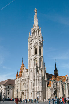 Vertical view of magnificent Gothic cathedral with colorful ceramic tile roof and tourists in foreground