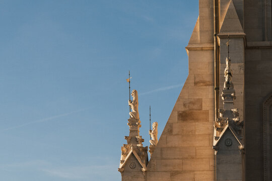 Close architectural view of carved stone gargoyle figures holding metal staffs on an ornate Gothic Revival building