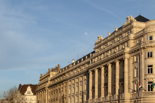 Elegant historic stone building with tall classical columns, ornate sculptures and balustrades illuminated by golden evening light
