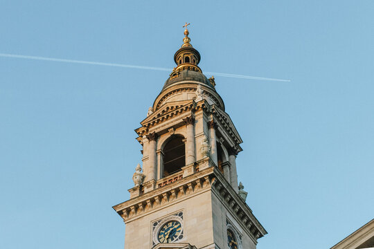 Ornate historic basilica bell tower and clock illuminated by warm evening sunlight against clear blue sky