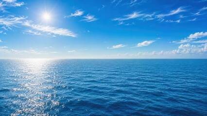 Naklejka premium Bright sun shines over a vast, calm ocean under a blue sky with scattered clouds.