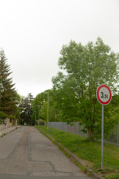 A quiet residential street lined with mature deciduous trees and a metal fence. A circular weight limit sign reading 3,5t stands on a roadside post in the