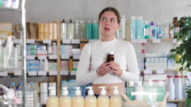 Young woman holds a bottle of medicinal syrup in her hands in a bird. Customer chooses medicines for a sore throat and colds. High quality 4k footage