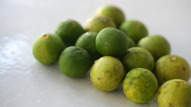 Fresh green and yellow limes arranged on a white surface, showcasing their natural texture and vibrant appearance. The citrus fruits display freshness and organic quality, making the image suitable