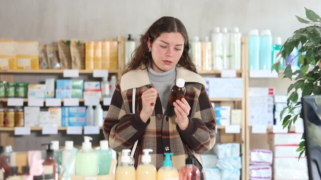 Young woman buyer chooses medicinal syrup in pharmacy