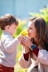 Obraz premium Child offering bright yellow flowers to his mother in a warm, sunlit outdoor moment