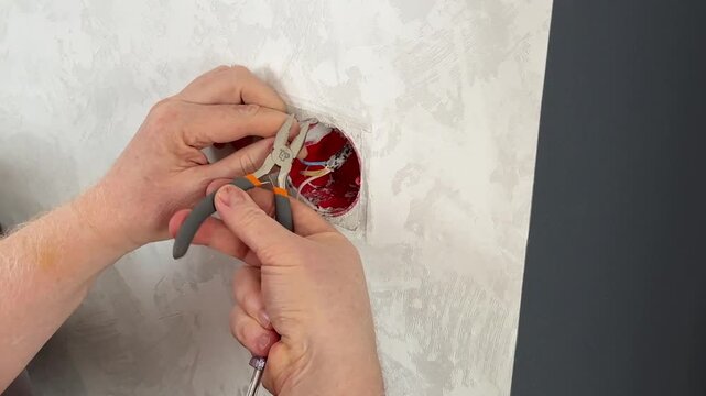 The electrician installs the outlet using pliers. Cutting the wires in the outlet