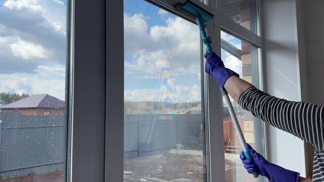 Woman in purple gloves cleans a window with a window cleaning mop